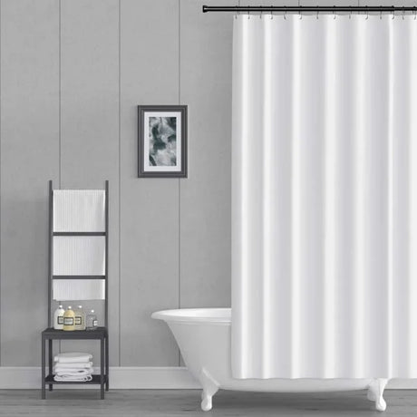 A white fabric shower curtain hanging from a black rod in a modern bathroom setting with a white clawfoot tub, a gray paneled wall, and a small black shelving unit.