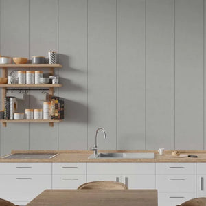 A modern kitchen interior with white cabinets, a light wood countertop, a built-in sink and faucet, open wooden shelves with jars and books, and a gray paneled wall behind.