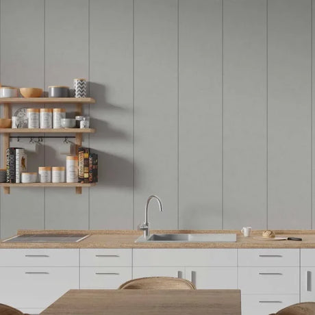 A modern kitchen interior with white cabinets, a light wood countertop, a built-in sink and faucet, open wooden shelves with jars and books, and a gray paneled wall behind.