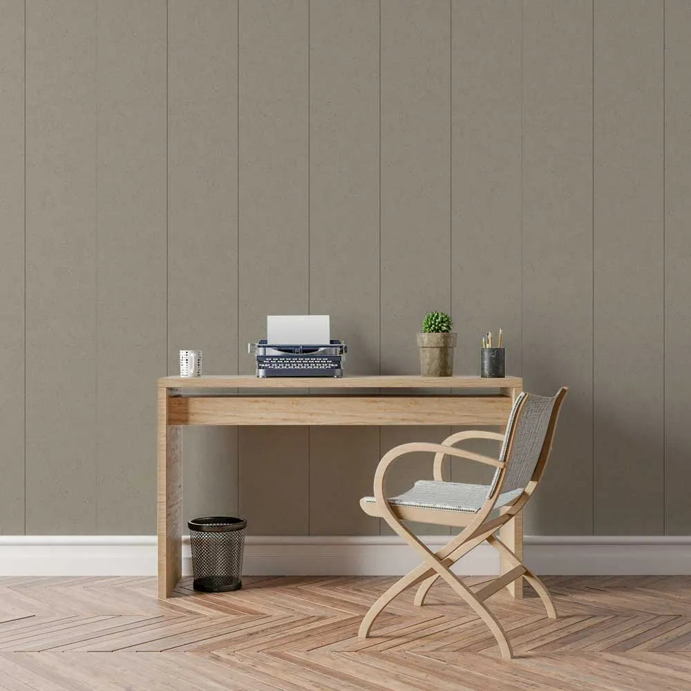 A styled interior scene showing a light wood desk against a taupe paneled wall, with a wooden folding chair, a small potted plant, a typewriter, and a small cup on top. The floor is herringbone wood.