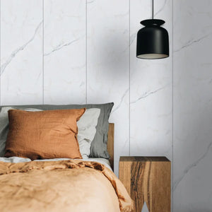 Bedroom with a bed, pillows, and a black pendant light against a marble wall.