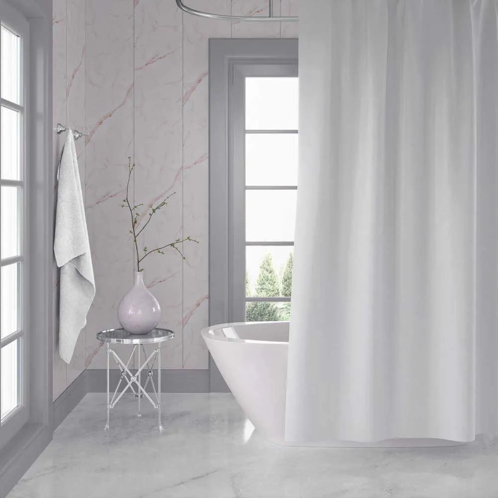A white fabric shower curtain hanging in a bright, modern bathroom with light marble walls and floor, a freestanding white tub, and a small side table with a vase.