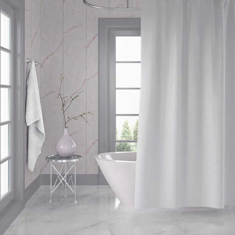 A white fabric shower curtain hanging in a bright, modern bathroom with light marble walls and floor, a freestanding white tub, and a small side table with a vase.