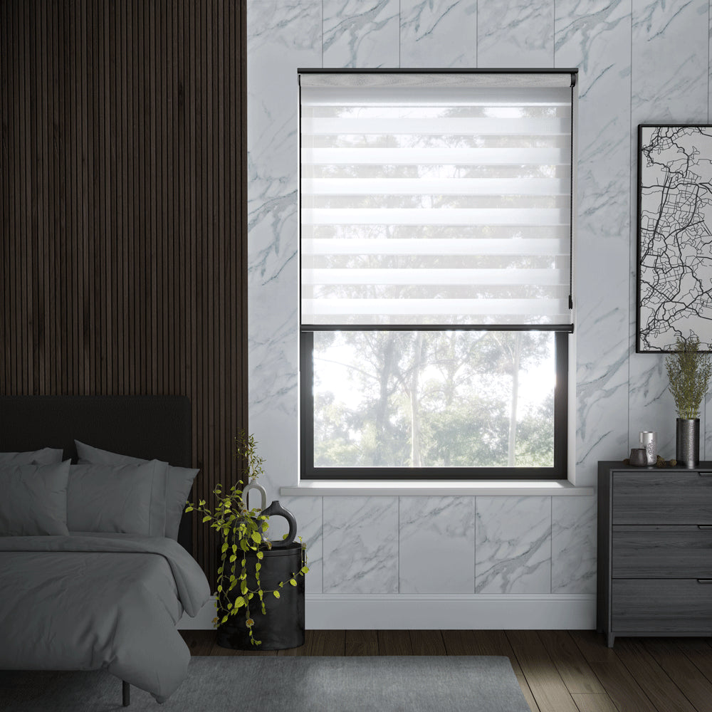 A modern bedroom interior featuring a window with a white roller blind, set against a white marble-patterned wall. The room also includes a dark wood slatted accent wall, a bed with gray bedding, a gray dresser, and a small potted plant.