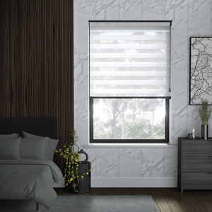 A modern bedroom interior featuring a window with a white roller blind, set against a white marble-patterned wall. The room also includes a dark wood slatted accent wall, a bed with gray bedding, a gray dresser, and a small potted plant.