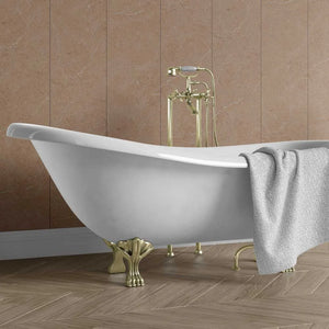 A white freestanding clawfoot bathtub with gold-tone legs and a matching gold faucet, shown in a bathroom setting with brown tiled walls and wood flooring. A gray towel is draped over the side.