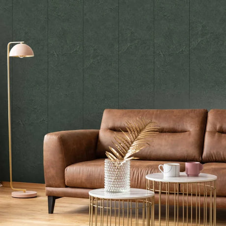 A styled living room scene featuring a brown leather sofa against a dark textured wall, with a gold floor lamp, two round gold wire coffee tables, and a vase with dried palm leaves.