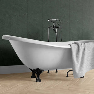A freestanding white clawfoot bathtub with black metal feet and a matching black faucet set, shown in a bathroom with dark green paneled walls and light wood flooring. A light gray towel is draped over the side of the tub.