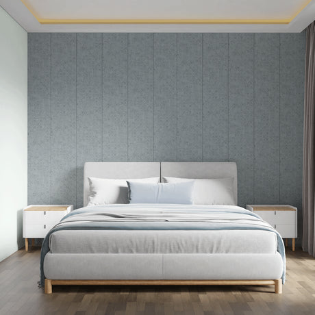 A modern bedroom featuring a light gray upholstered bed frame with a wooden base, styled with white and light blue bedding. The bed is centered against a textured gray paneled wall, flanked by two white nightstands with light wood tops, on a dark wood floor.