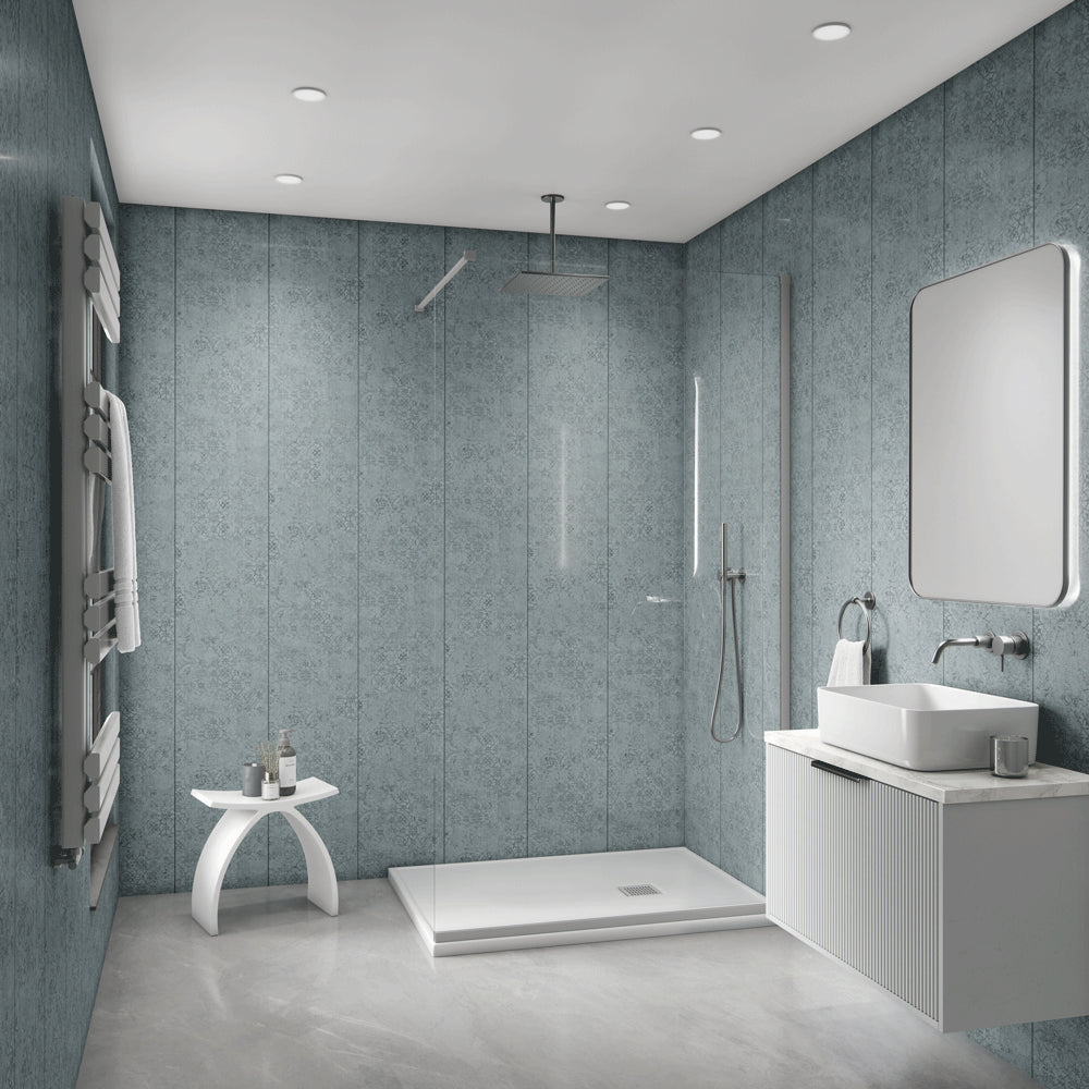 A modern bathroom interior with blue-gray textured wall panels, a glass shower enclosure, white vessel sink, floating vanity, and a small white side table with towels.