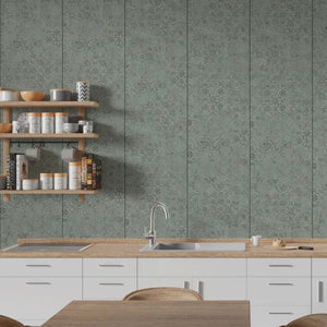 A modern kitchen interior featuring sage green patterned wall panels behind white cabinets and a light wood countertop with a sink and faucet. Floating wooden shelves on the left hold jars, bowls, and books.