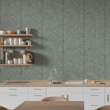 A modern kitchen interior featuring sage green patterned wall panels behind white cabinets and a light wood countertop with a sink and faucet. Floating wooden shelves on the left hold jars, bowls, and books.