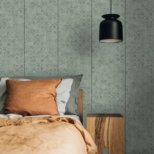 A styled bedroom corner featuring textured sage green vertical wood-look wallpaper, a black pendant light, a wooden nightstand, and bedding with a rust-orange pillow.