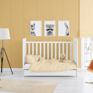 A styled nursery room featuring a white wooden toddler bed with pale yellow bedding and a teddy bear, set against a mustard yellow paneled wall with three framed black and white animal prints above.