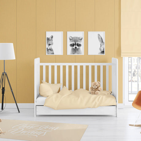 A styled nursery room featuring a white wooden toddler bed with pale yellow bedding and a teddy bear, set against a mustard yellow paneled wall with three framed black and white animal prints above.