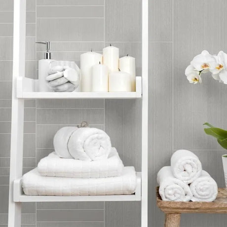 Bathroom with white towels, candles, and a plant on a gray tiled wall background