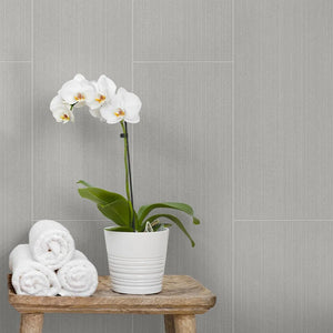 White orchid in a pot on a wooden stool against a gray tiled wall