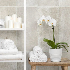 Bathroom setting with white towels, candles, and a potted orchid on a wooden stool.