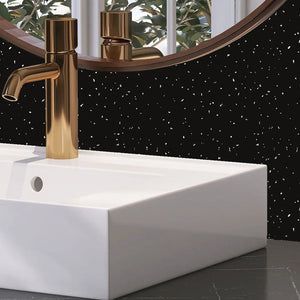 A modern bathroom scene featuring a matte gold single-handle faucet mounted on a white rectangular vessel sink, set against a black wall with white speckles and a round mirror.