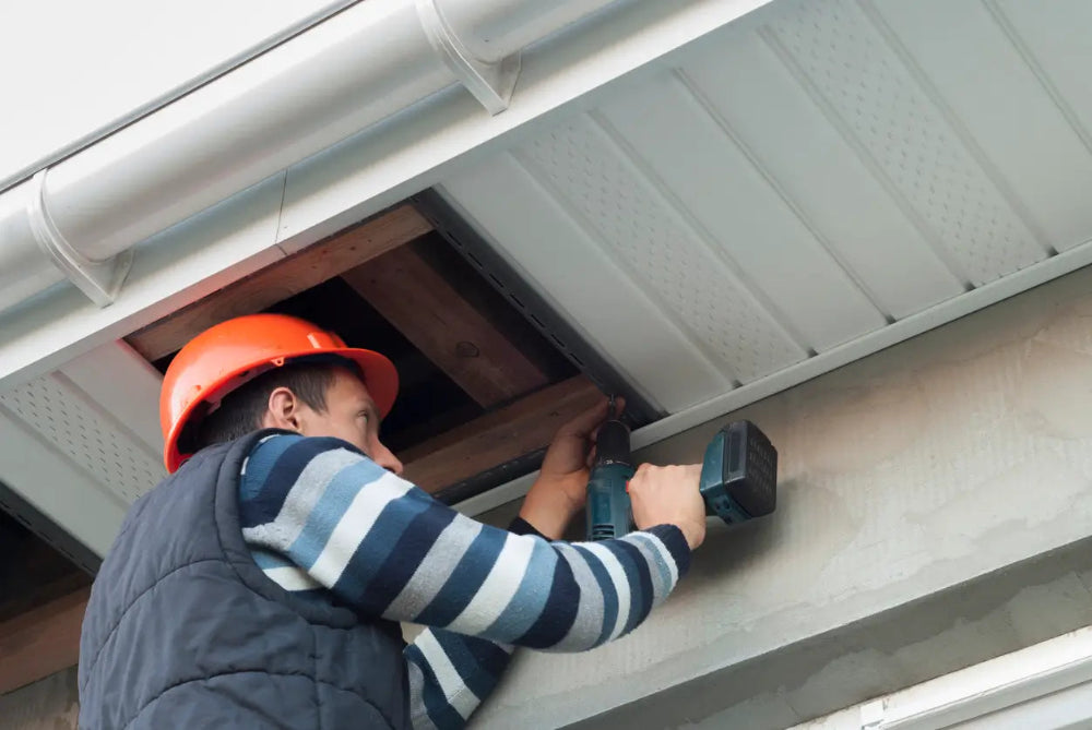 Person working on a roof with a tool, wearing a hard hat and striped shirt.