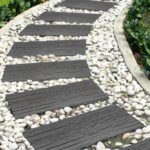 Dark gray rectangular stepping stones with a wood-grain texture, arranged in a curved garden path over white pebbles.